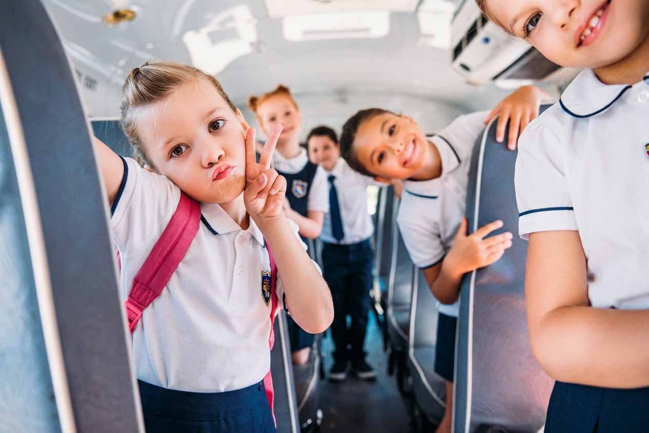 Young learners in school uniform laughing and pulling playful faces aboard a Beremi scholar bus